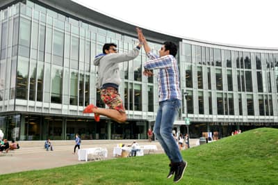 Zwei internationale Studenten geben sich High-Five während eines Luftsprungs auf dem Campus der TRU