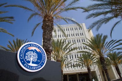 Campusgebäude der CSU Fullerton mit Uni-Logo im Vordergrund und zahlreichen Palmen.
