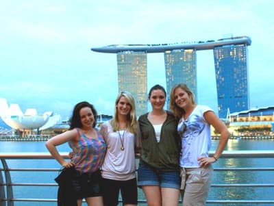 Internationale Studentinnen posieren an der Uferpromenade vor dem Panorama des leuchtenden Marina Bay Sands Hotels