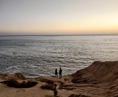 Zwei Personen stehen auf einer Felsenklippe an der Küste bei Sonnenuntergang
