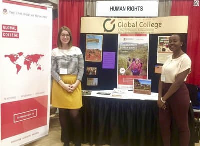 Zwei Studentinnen stellen mit einem Stand das Global College und den Bachelor of Human Rights vor.