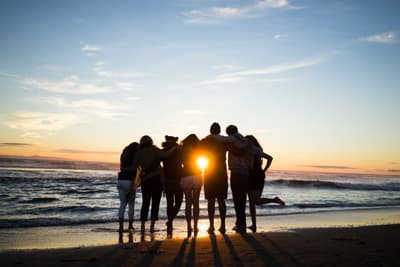 Eine Gruppe von Studierenden bewundert Arm in Arm den Sonnenuntergang über dem Meer.