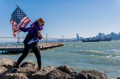 Frau mit amerikanischer Flagge vor der Skyline von San Francisco (USA)