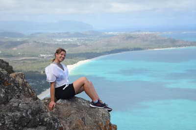 Studentin sitzt auf einem Felsen und ist umgeben von der traumhaften Landschaft in Hawaii