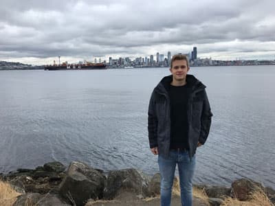 Ein junger Mann steht vor einem Hafen, im Hintergrund sieht man Hochhäuser