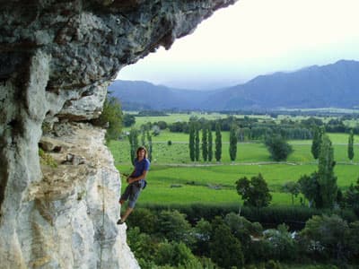 Student klettert weit oben auf einem Felsen vor sehr grüner Landschaft