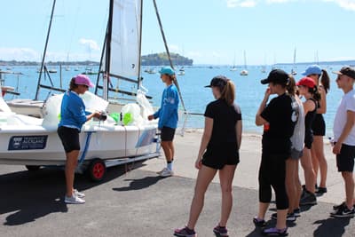 Einer Gruppe von Studenten wird im Hafen das Trainings-Segelboot erklärt
