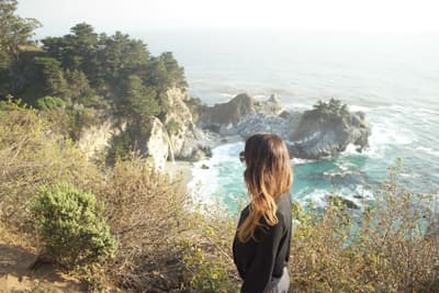 Studentin vor einer felsigen und grün bewachsenen Küstenlandschaft in Kalifornien