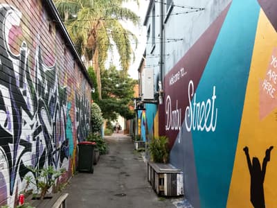 Graffiti-bemalte Wände mit Palmenpanorama, Sitzgelegenheiten und Lichterkette in einer kleinen Seitenstraße der hippen Darby Street