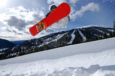 Sprung mit einem roten Snowboard bei strahlendem Sonnenschein in Sun Peaks