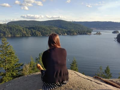 Eine Studentin sitzt auf einem Felsen und genießt den Ausblick über den Ozean und zahlreiche kleine bewaldete Inseln