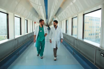 Zwei Personen in Arztkittel laufen durch einen weißen Gang, der zwei Gebäude verbindet