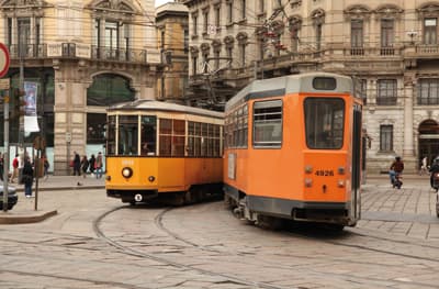 Zwei historisch aussehende Straßenbahnen begegnen sich in den mit prachtvollen Altbauten gesäumten Straßen Mailands