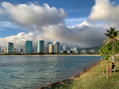 Blick von einer grünen Uferpromenade über das Wasser auf die Skyline von Honolulu
