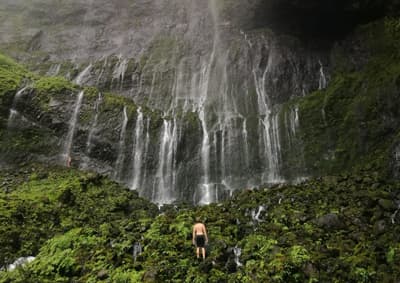 Student vor einem sehr hohen, verzweigten Wasserfall, der über bemooste Felsen hinabfällt