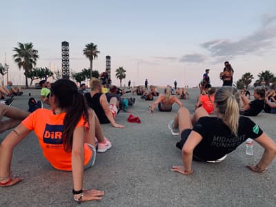 Dynamisches Bild einer Laufgruppe, die in der Nähe des Strandes Aufwärmübungen im Freien bei Abendstimmung macht 