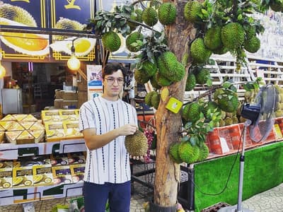 Ibrahim in einem Obstgeschäft, wo die charakteristische Durianfrucht verkauft wird. Sie ist groß, grün und stachelig.