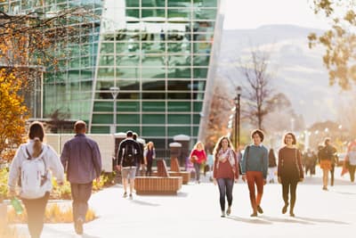 Studenten laufen über den Campus der University of Otago, vorbei an einem modernen Gebäude mit Glasfassade.
