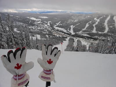 Schneehandschuhe mit kanadischem Ahornblatt vor dem Panorama der verschiedenen Abfahrten des Sun Peaks Skigebiets