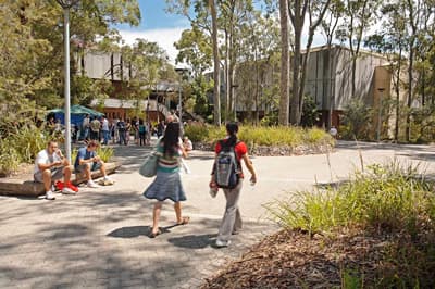 2 Studentinnen laufen über den belebten und grünen Campus der University of Newcastle