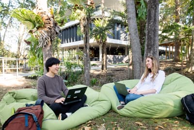 zwei Studierende sitzen beim Lernen draußen auf dem Campusgelände der Southern Cross University in Lismore 
