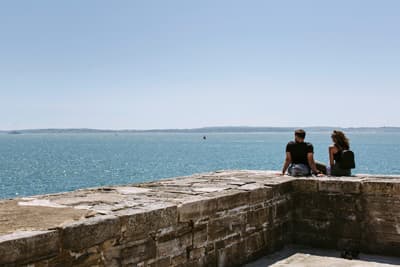 Zwei Studierende sitzen auf einer alten Kaimauer und blicken aufs Meer