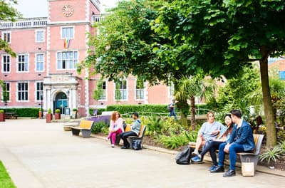 Studierende sitzen auf einer Bank auf dem Campus