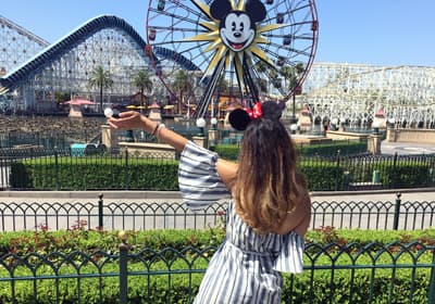 Studentin posiert mit Mickeymausohren vor Fahrgeschäften im kalifornischen Disneyland.