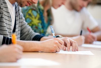 Student schreibt auf ein Blatt Papier während eines Zulassungstests.