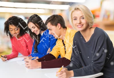 Eine junge Frau neben einer Gruppe Studierender lächelt in die Kamera.