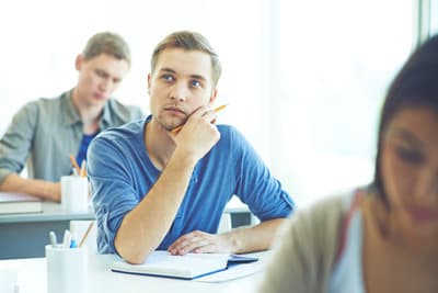 Student sitzt am Tisch und denkt nach