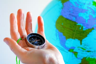 Hand mit Kompass vor einem Globus mit dem Ausschnitt Nordamerika