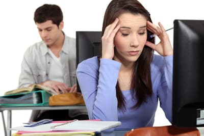 Junge Frau mit Kopfschmerzen vor einem Computer