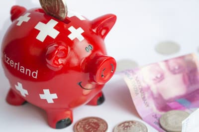 Sparschwein mit Schweizer Flagge umgeben von Geldscheinen und Münzen