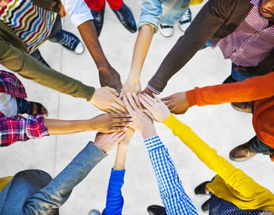Menschen mit unterschiedlichen Hautfarben stehen im Kreis und legen die Hände aufeinander.