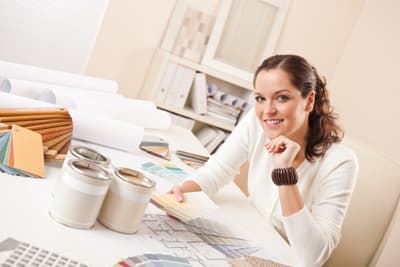 Frau sitzt lächelnd am Schreibtisch mit künstlerischem Arbeitsmaterial