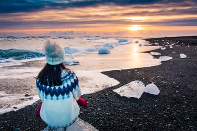 Frau sitzt auf einem Eisberg und genießt den Sonnenuntergang am Diamond Beach in Island