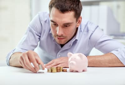 Mann zählt Münzen auf dem Tisch neben einem Sparschwein