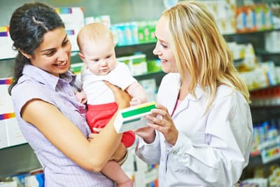 Frau mit Baby auf dem Arm lässt sich in einer Apotheke beraten