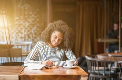 Studentin schreibt in ein Notizbuch in einem Café