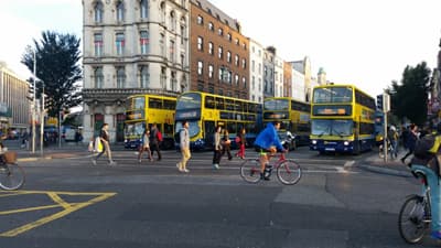 Straßenansicht mit Fußgängern, Fahrradfahrern und Bussen
