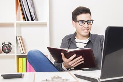 Student sitzt mit einem Buch vor dem Laptop