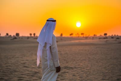 Mann in weißer Kleidung in einer Wüste bei Sonnenuntergang