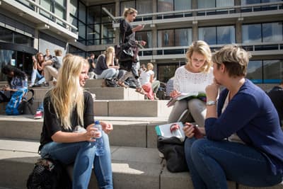 Studierende sitzen auf einer Treppe und unterhalten sich