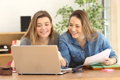 Zwei Studentinnen sitzen fröhlich vor dem Laptop