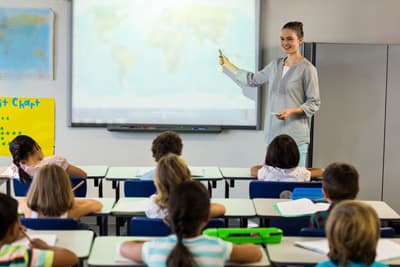 Eine junge Lehrerin steht vor einer Klasse und zeigt auf eine Landkarte.