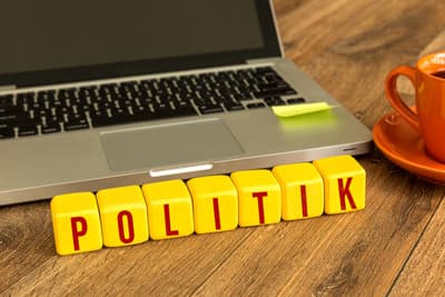 Schriftzug "Politik" in Form von Buchstabenwürfeln vor einem aufgeklappten Laptop