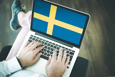 Ein Student hat einen Laptop auf dem Schoß, den Bildschirm ziert die schwedische Flagge.