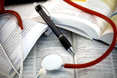 Ein Kugelschreiber und ein Stethoskop liegen auf medizinischen Lehrbüchern.