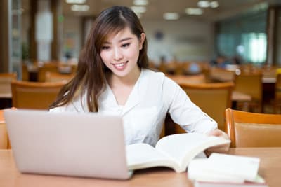 Eine lächelnde Studentin sitzt am Laptop.